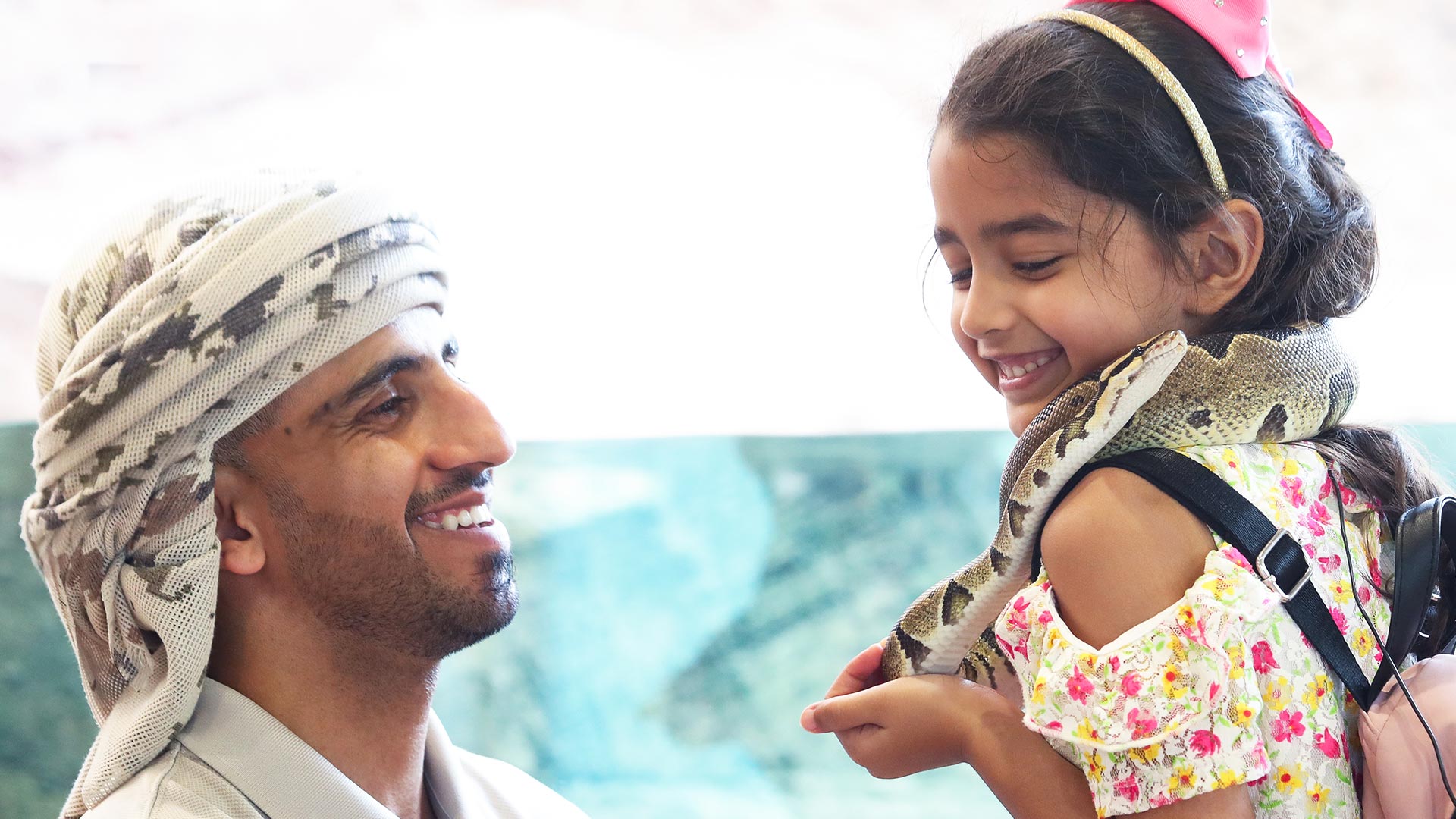 A little girl holding a python wrapped around her neck whilst being assisted by an animal specialist at Al Ain Zoo.