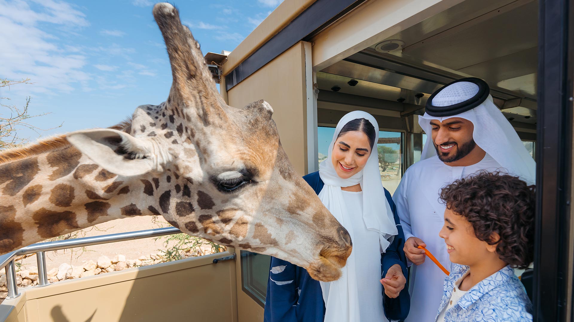 An Emirati family feeding a giraffe with a carrot
