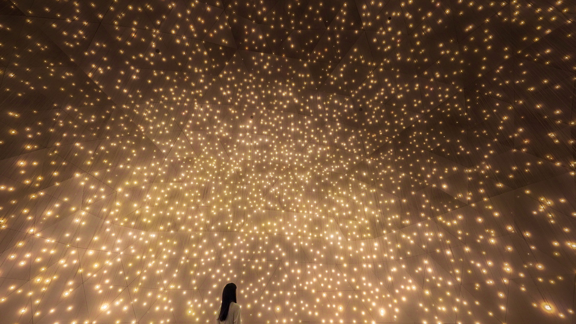 A lady wearing a white dress glazing up looking at bright yellow particles that look like little suns